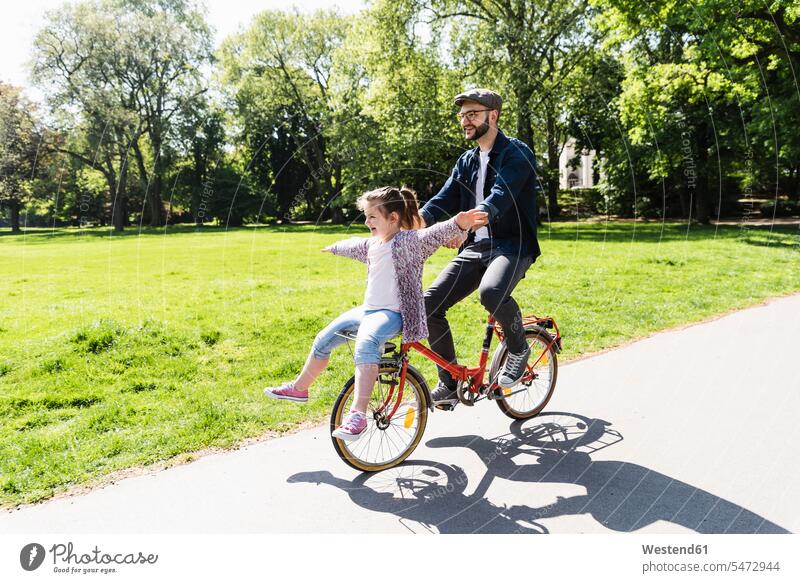Happy father riding bicycle with daughter in a park bikes bicycles riding bike bike riding cycling bicycling pedaling active daughters parks fathers daddy dads