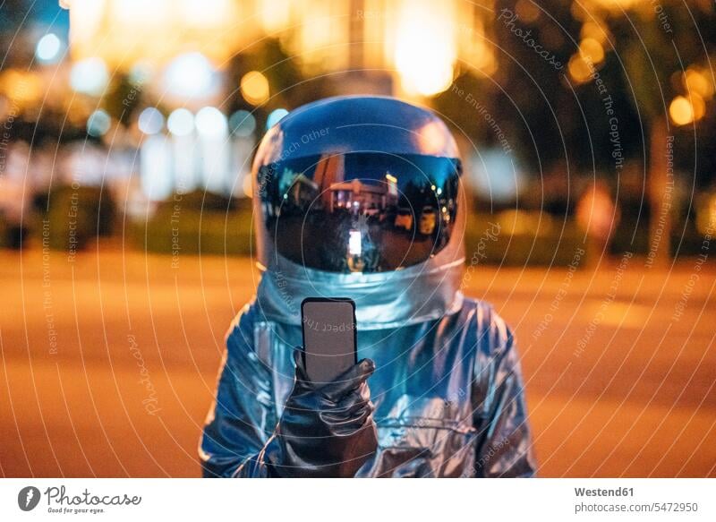 Spaceman on a street in the city at night holding smartphone town cities towns mobile phone mobiles mobile phones Cellphone cell phone cell phones astronaut