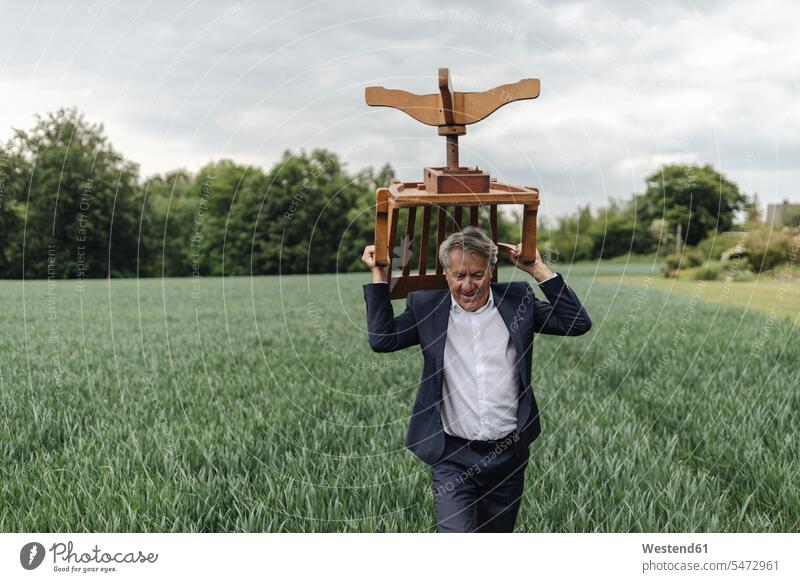 Senior businessman carrying a chair on a field in the countryside business life business world business person businesspeople Business man Business men