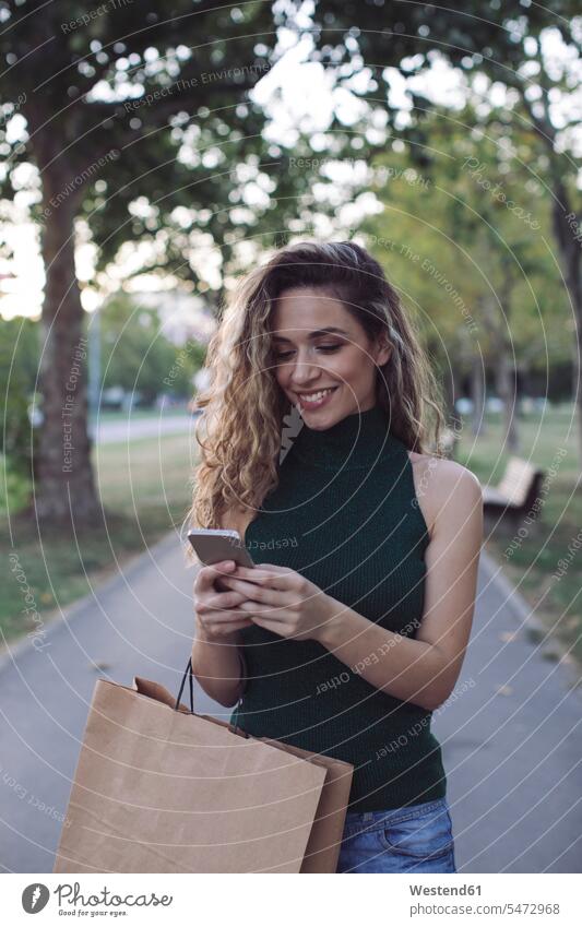 Smiling woman using smart phone in public park color image colour image outdoors location shots outdoor shot outdoor shots day daylight shot daylight shots