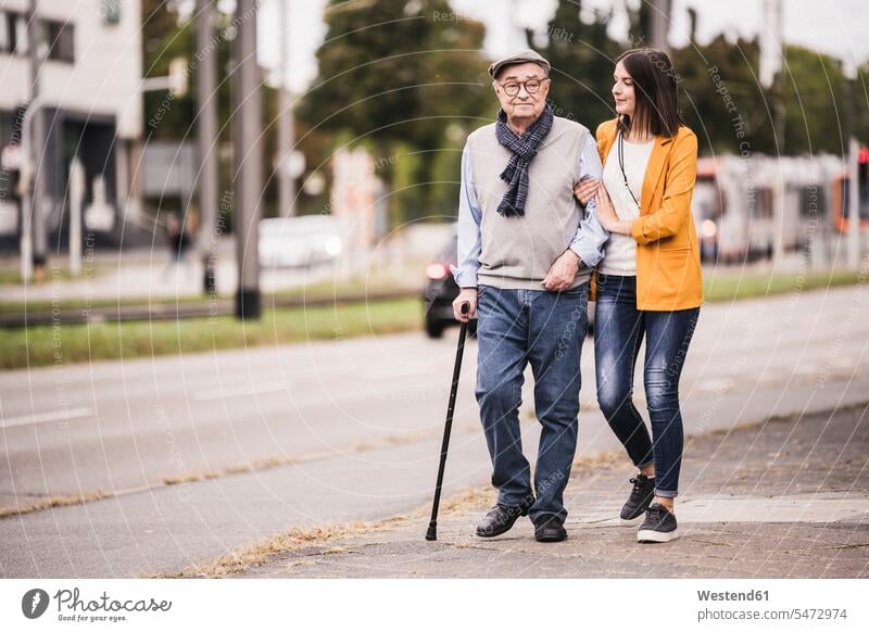 Adult granddaughter assisting her grandfather strolling with walking stick generation go going free time leisure time Lifestyle location shot location shots