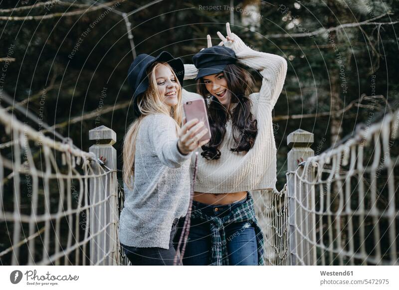 Two happy young women on a suspension bridge taking a selfie happiness woman females female friends Selfie Selfies bridges Adults grown-ups grownups adult