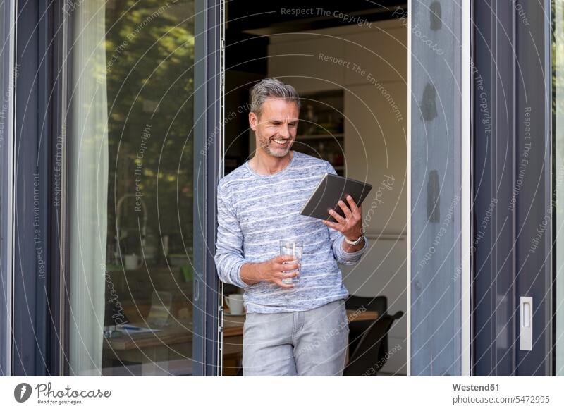 Smiling mature standing at French door at home using a tablet French Door smiling smile man men males digitizer Tablet Computer Tablet PC Tablet Computers iPad