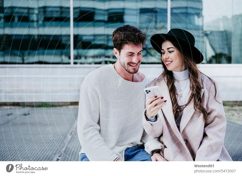 Smiling woman showing smart phone to male partner in city color image colour image outdoors location shots outdoor shot outdoor shots day daylight shot