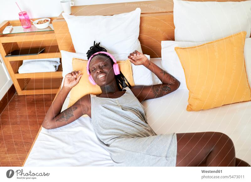 Woman listening music through headphones while relaxing on bed at home color image colour image indoors indoor shot indoor shots interior interior view