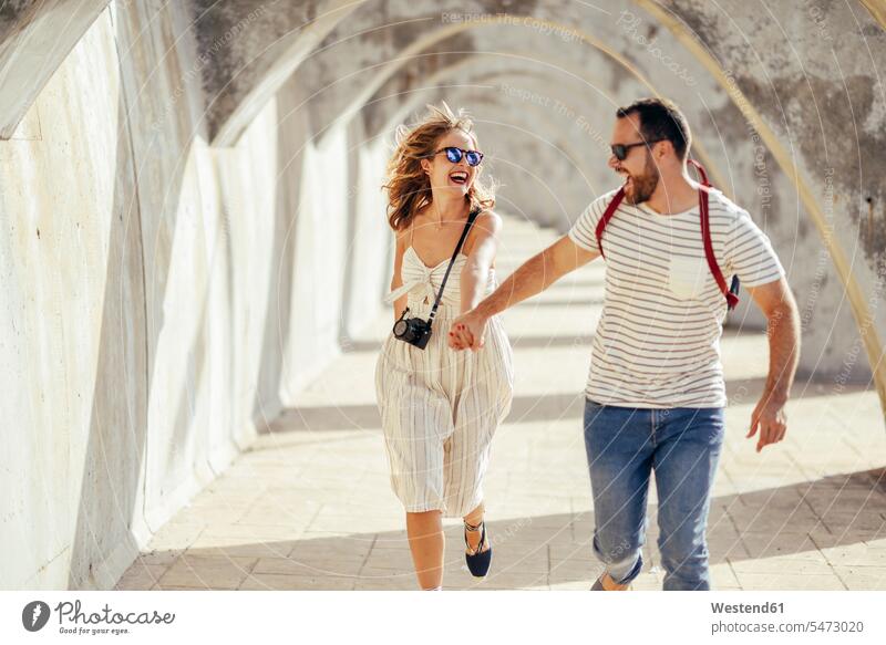 Spain, Andalusia, Malaga, carefree tourist couple running under an archway in the city town cities towns twosomes partnership couples tourists outdoors