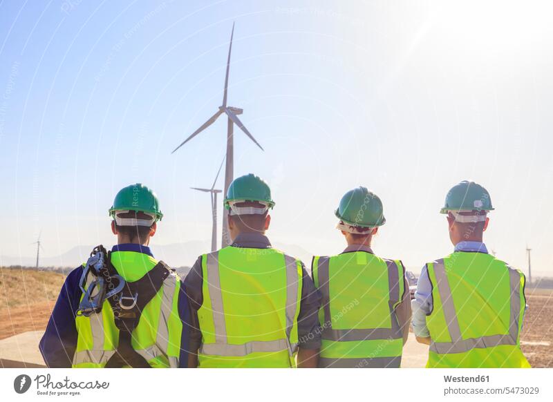 Rear view of four engineers on a wind farm wind park technology technologies engineering wind power plant wind turbine wind turbines wind energy