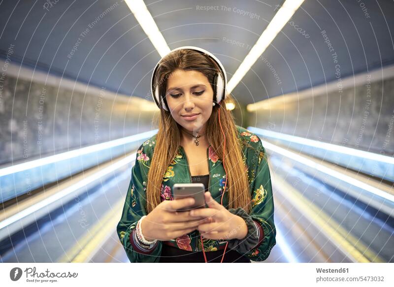 Portrait of woman with headphones looking at cell phone in underground station underground stations subway stations headset Smartphone iPhone Smartphones