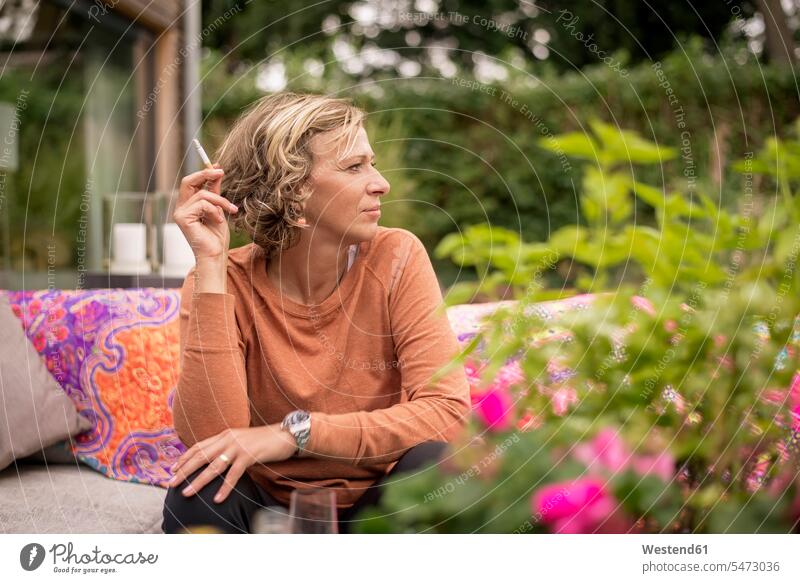 Woman holding cigarette while sitting on sofa at backyard color image colour image day daylight shot daylight shots day shots daytime casual clothing