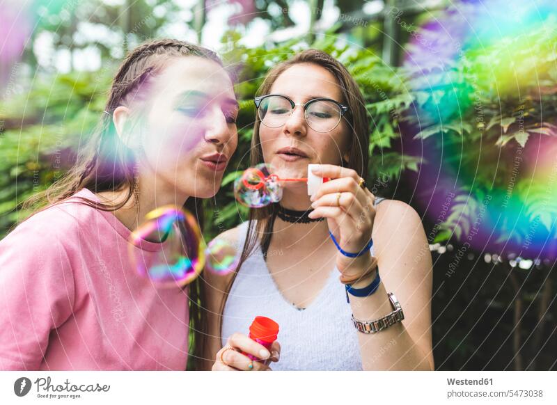 Two teenage girls blowing soap bubbles together female friends woman females women Teenage Girls female teenagers mate friendship Adults grown-ups grownups