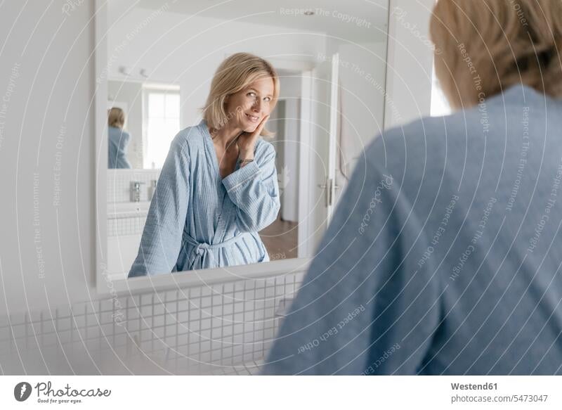 Portrait of smiling mature woman looking in bathroom mirror smile females women portrait portraits watching Domestic Bathroom bath room mirrors Adults grown-ups