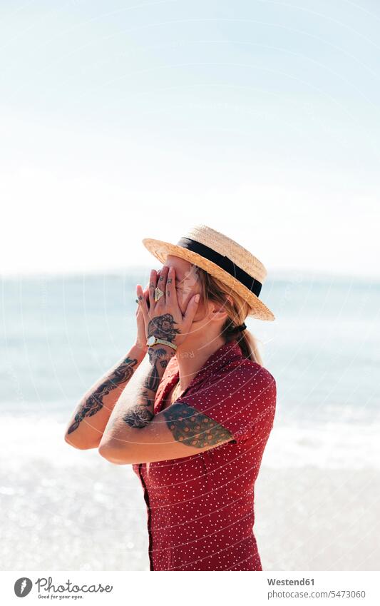 Young woman with tattoos on hand and arms covering her face in front of the sea females women human hand hands human hands Sea ocean tattooed body art