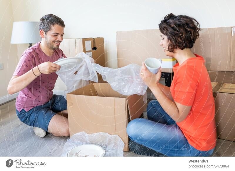 Happy couple moving into new home unpacking cardboard box Crockery Tableware cup mugs cardboard boxes Cardboard Carton Cardboards cardbox cardboxes carton