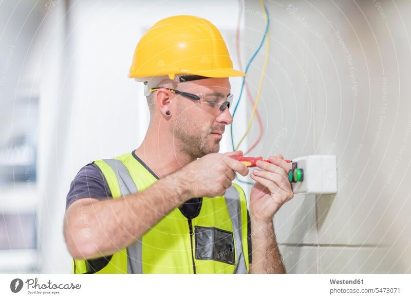 Electrician screwing in wire on construction site Building Site sites Building Sites construction sites cable power cord cables constructing Safety Helmet