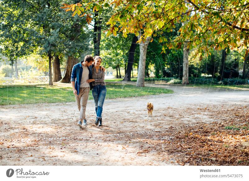 Happy young couple with dog in a park animals creature creatures domestic animal pet Canine dogs relax relaxing go going walk smile embrace Embracement hug