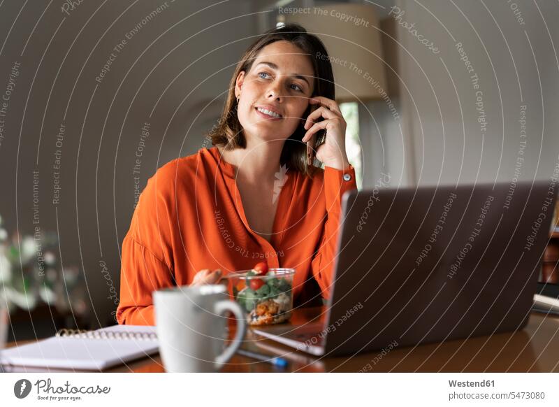 Smiling businesswoman talking on mobile phone while eating salad at home color image colour image indoors indoor shot indoor shots interior interior view