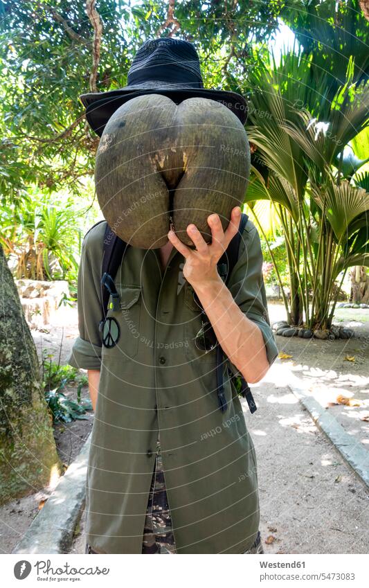 Seychelles, man hiding his face behind huge seed of Coco de Mer hat hats copy space impressive monumental recreation relaxing Recreational obscured face