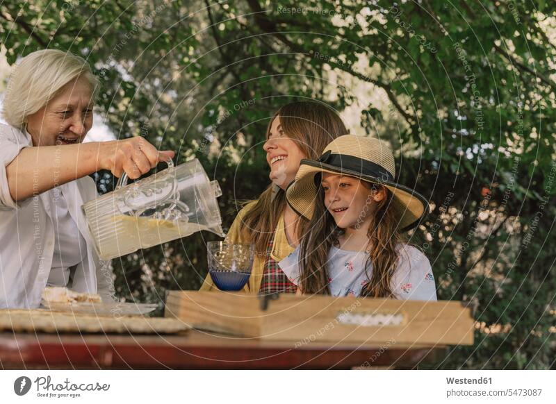 Senior woman pouring drink for daughter and granddaughter in glass at yard color image colour image Spain leisure activity leisure activities free time