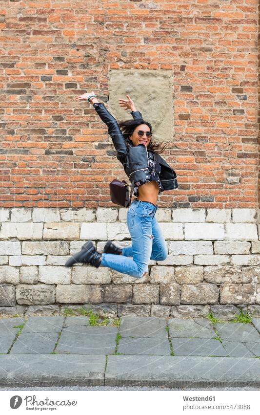 Young woman jumping in the air, brick wall in the background jump in the air nonconformist unadapted nonconformity females women Leaping leather jacket