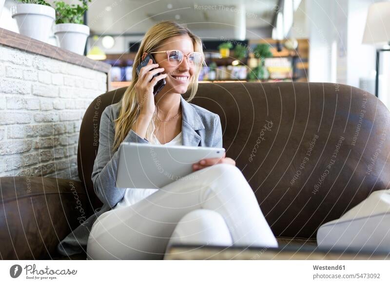 Young woman talking on mobile phone while using her digital tablet in a coffee shop business life business world business person businesspeople business woman