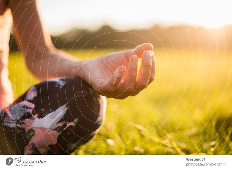 Detail of woman in lotus position on rural meadow at sunset country countryside sunsets sundown females women yoga meadows atmosphere atmospheric mood moody