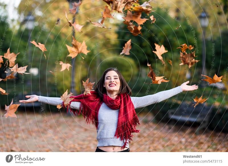 Portrait of laughing young woman with red scarf throwing autumn leaves in the air scarfs scarves females women portrait portraits autumn foliage fall happiness