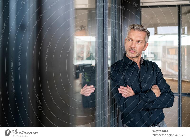 Buinessman standing in office, leaning on glass wall, thinking, with arms crossed human human being human beings humans person persons caucasian appearance