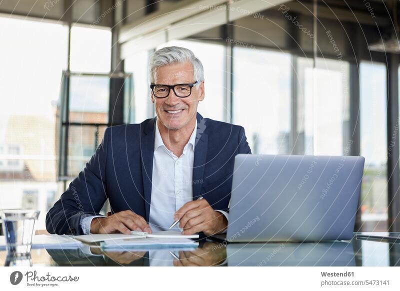 Businessman working at laptop, taking notes in notebook mature men mature man Business man Businessmen Business men desk desks using laptop using a laptop
