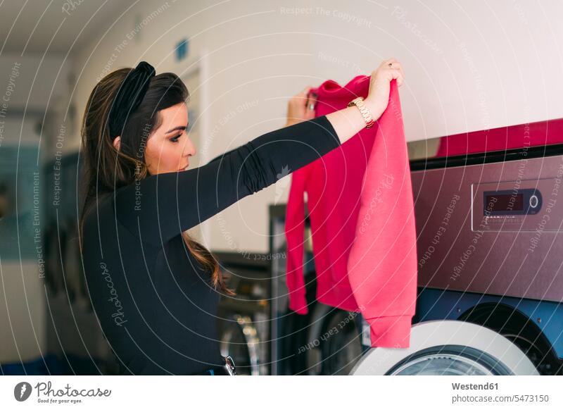 Young woman doing the laundry in a launderette looking at pink sweatshirt human human being human beings humans person persons caucasian appearance