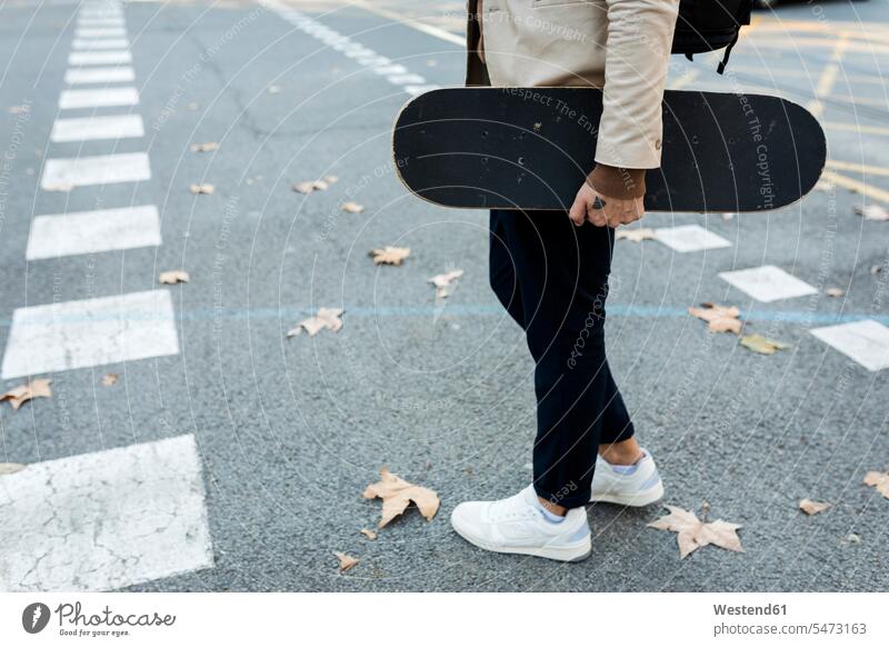 Man with backpack and skateboard crossing the street in autumn, partial view man men males rucksacks backpacks back-packs Skate Board skateboards fall road