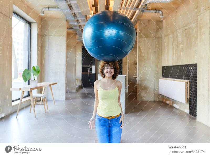 Portrait of smiling woman balancing a fitness ball on her head nonconformist unadapted nonconformity Germany break room businesswoman businesswomen