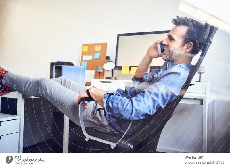 Relaxed man sitting at desk in office talking on cell phone on the phone call telephoning On The Telephone calling Seated mobile phone mobiles mobile phones