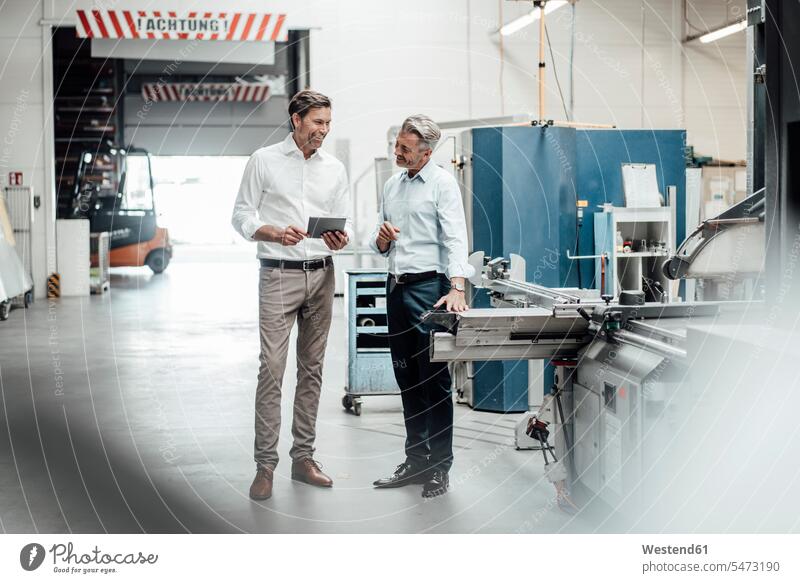 Happy mature businessmen discussing while standing in factory color image colour image Germany indoors indoor shot indoor shots interior interior view Interiors