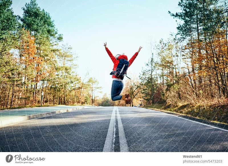 Cheerful woman jumping on an empty road during backpacking trip cheerful gaiety Joyous glad Cheerfulness exhilaration merry gay rucksacks backpacks back-packs