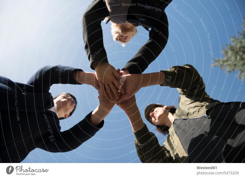 Worm's eye view of three women stacking their hands under blue sky female friends togetherness Unity United piling pile helpfulness solidarity unity Part Of
