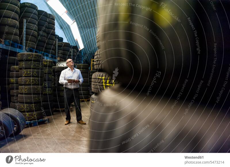 Senior businessman looking up while standing with digital tablet amidst tires color image colour image indoors indoor shot indoor shots interior interior view