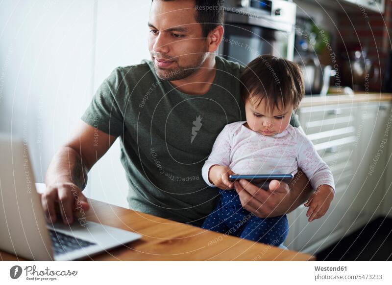 Father using laptop with baby girl using smartphone at home Laptop Computers laptops notebook daughter daughters father pa fathers daddy dads papa infants