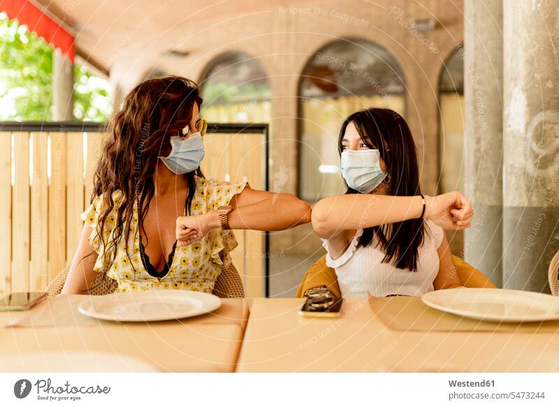 Young women wearing masks while greeting with elbow bump in restaurant color image colour image Spain indoors indoor shot indoor shots interior interior view