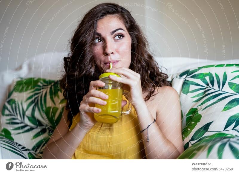Beautiful young woman with long brown hair sipping juice from straw in mason jar while looking away color image colour image Spain leisure activity