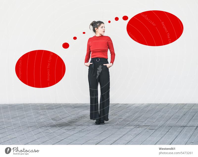 Young woman with hands in pockets standing against blank red speech bubble on wall color image colour image outdoors location shots outdoor shot outdoor shots