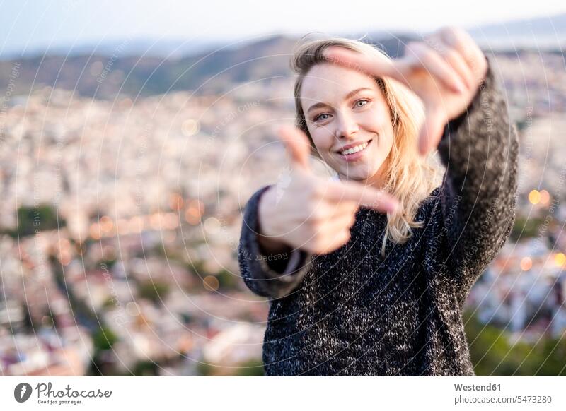 Portrait of young woman making a finger frame at sunrise above the city, Barcelona, Spain human human being human beings humans person persons