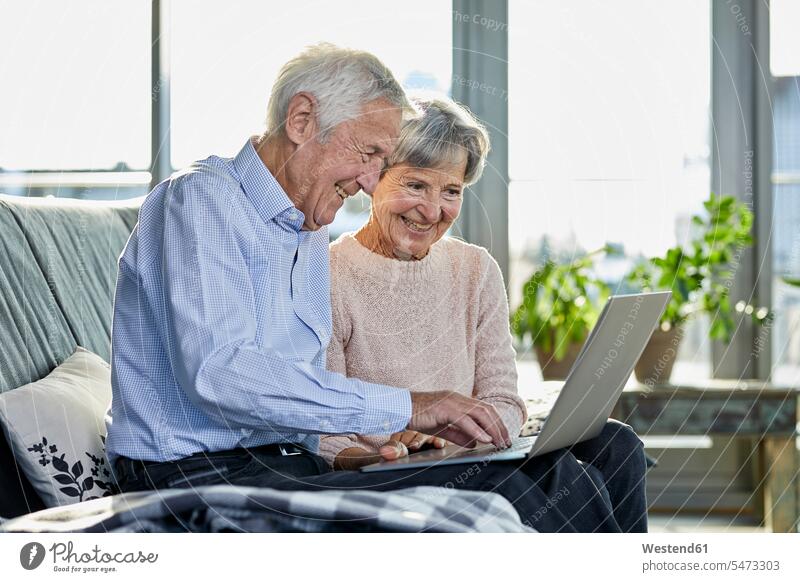 Senior couple sitting together on couch using laptop settee sofa sofas couches settees twosomes partnership couples senior couple elder couples senior couples