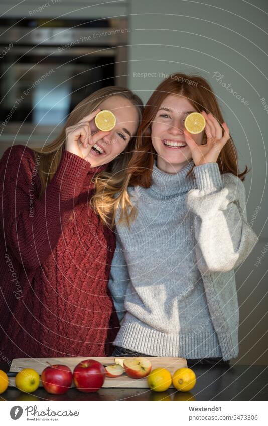 Two laughing friends holding lemon halves in front of their eyes female friends half halved Lemon Lemons mate friendship cross section cross sections