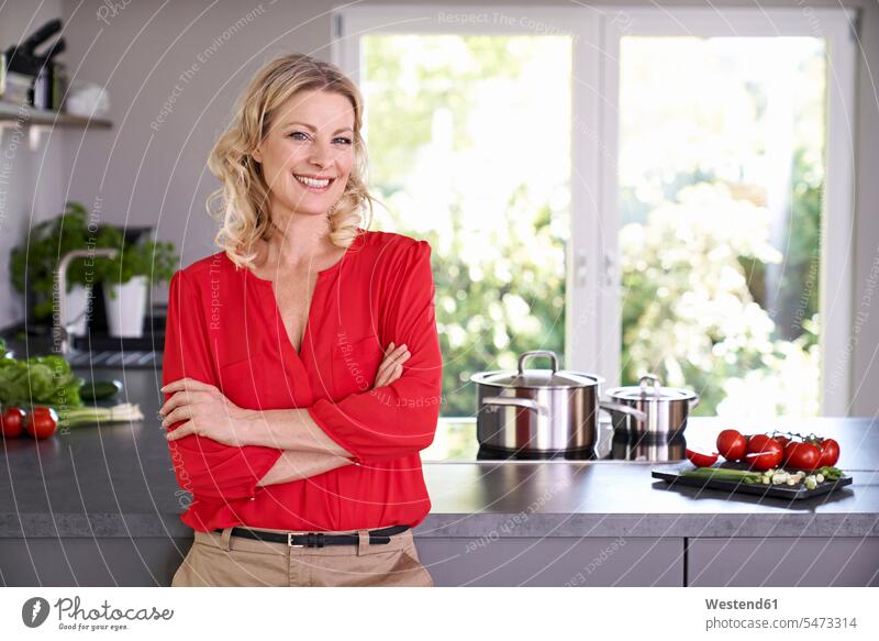 Portrait of smiling woman wearing red blouse standing in kitchen blouses portrait portraits domestic kitchen kitchens smile females women colour colours Adults