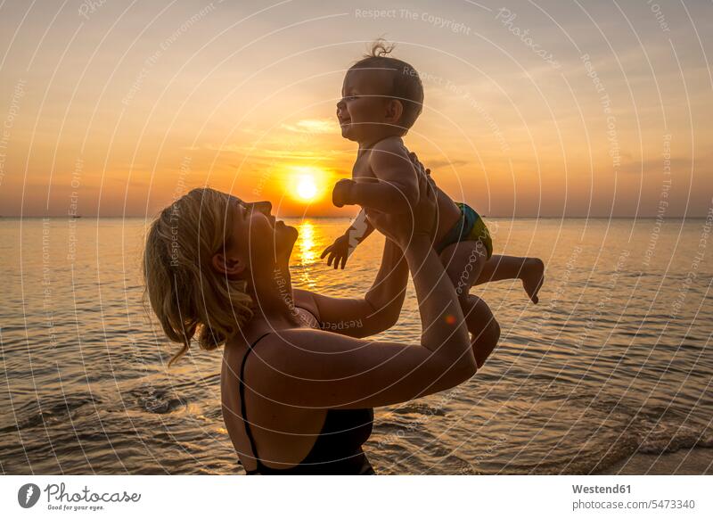 Vietnam, Phu Quoc island, Ong Lang beach, Mother holding baby in beach at sunset outdoors location shots outdoor shot outdoor shots sunsets sundown atmosphere