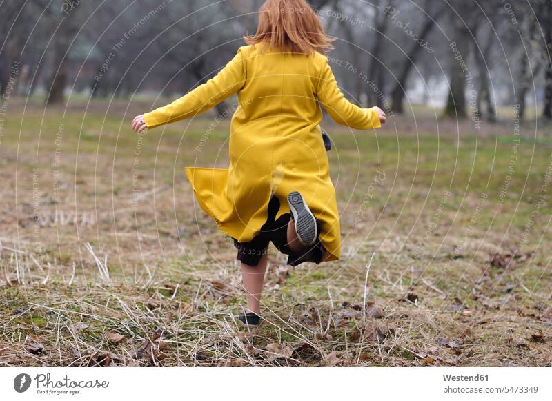 Rear view of woman in yellow coat running on grass at park color image colour image outdoors location shots outdoor shot outdoor shots day daylight shot