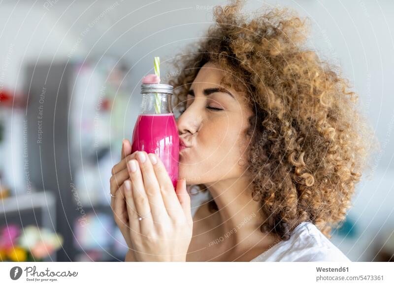 Woman kissing a smoothie glass at home human human being human beings humans person persons curl curled curls curly hair drinking straw drinking straws hold