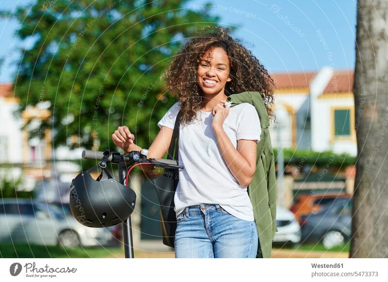Happy young woman carrying jacket while standing with electric push scooter during sunny day color image colour image outdoors location shots outdoor shot