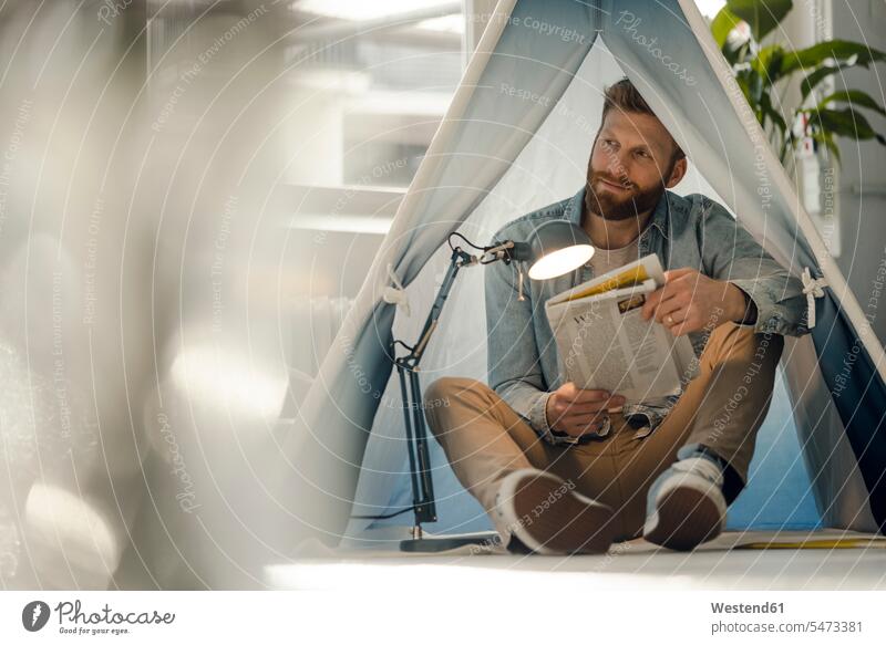 Man camping in his living room, reading the newspaper alone solitary solo man men males home at home newspapers tent tents Adults grown-ups grownups adult