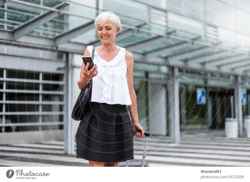 Smiling senior woman with baggage looking on cell phone smiling smile senior women elder women elder woman old mobile phone mobiles mobile phones Cellphone